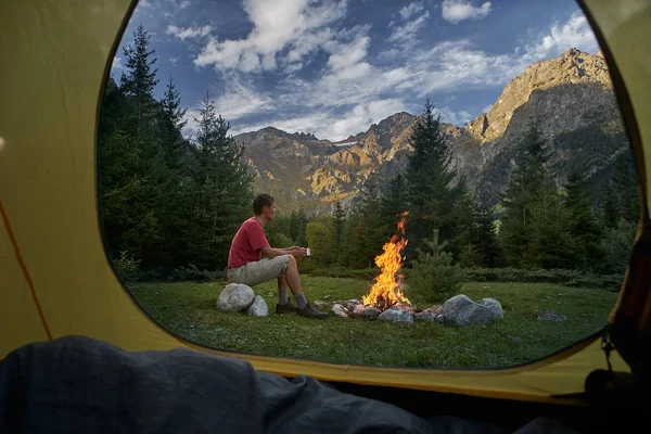 Visa från inne turist tältet vid solnedgången. Ensam turist, mannen hiker sitter vid brasan — Stockfoto
