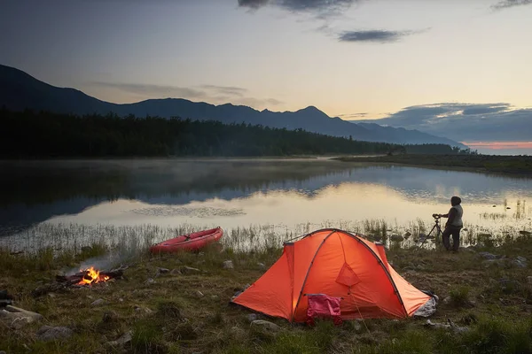 Fotograf tar en bild av vacker sjö och berg nära orange tält. — Stockfoto