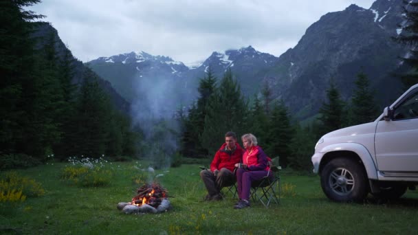 Çift karanlık bir dağ vadisinde bir kamp şenlik ateşi ile sohbet. Beyaz araba — Stok video