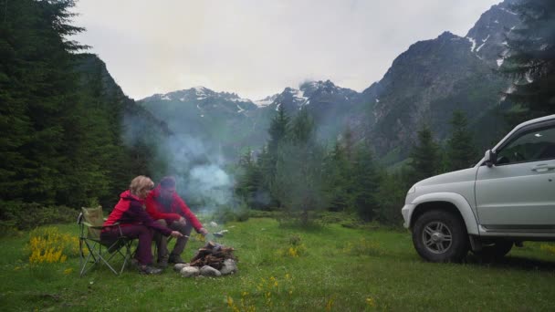 Çift karanlık bir dağ vadisinde bir kamp şenlik ateşi ile sohbet. Beyaz araba. — Stok video