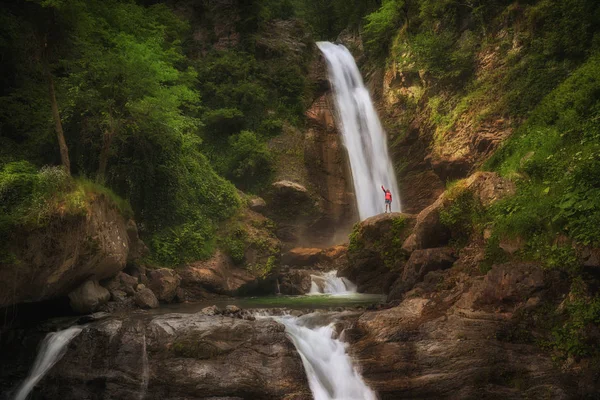 穿着红色夹克的徒步旅行妇女住在山上的大瀑布. 免版税图库图片