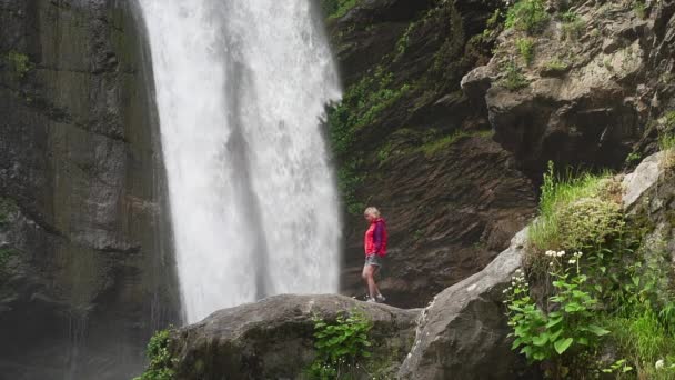 Wanderin in roter Jacke läuft in der Nähe des großen Wasserfalls — Stockvideo