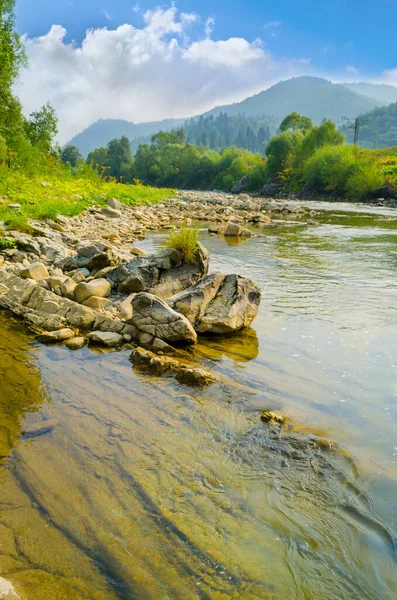 Arka planda dağlar olan kayalık kıyıları olan temiz bir nehir.