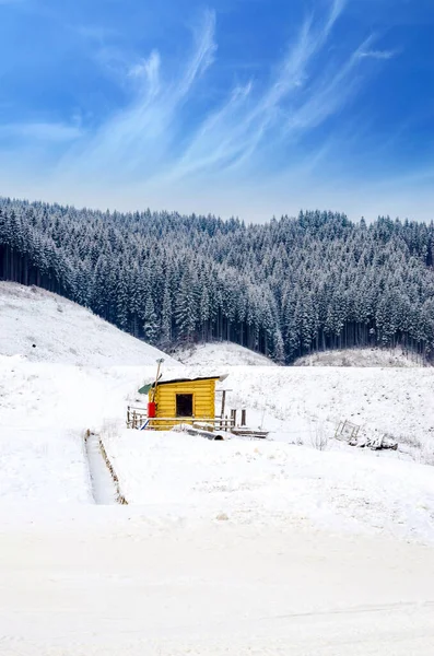 Karlı bir dağ yamacında küçük ahşap bir kulübesi olan kış manzarası