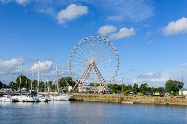 Nehir, mavi gökyüzü ve dönme dolabı olan şehir manzarası.