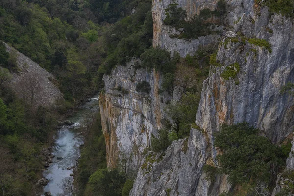Bulutlu bir günde kayalık uçurum, nehir ve dağ manzarası.