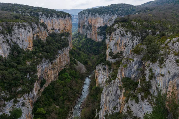 Bulutlu bir günde kayalık uçurum, nehir ve dağ manzarası.