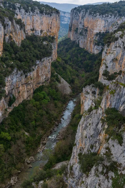 Bulutlu bir günde kayalık uçurum, nehir ve dağ manzarası.