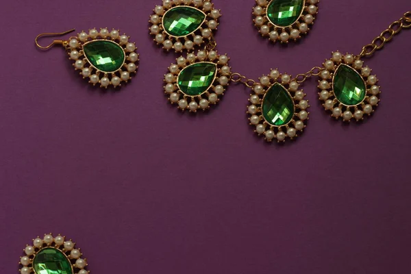 luxury green jewelry in the Baroque style on a purple background. Vintage, retro style.