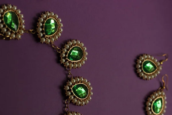 luxury green jewelry in the Baroque style on a purple background. Vintage, retro style.