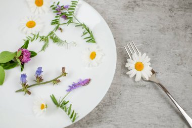 Gri desenli arka plan çatallı beyaz bir tabakta çiçekler ve yeşil bitki, vejetaryen gıda konsepti.
