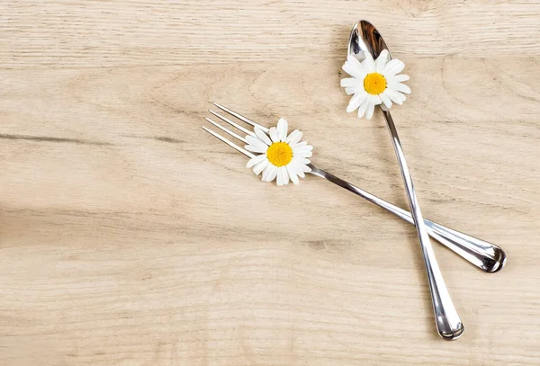 Koncepcja zdrowego odżywiania, widok z góry łyżki i widelec z kwiatami stokrotka na drewnianym tle — Zdjęcie stockowe
