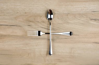 Crossed fork and spoon on wooden table clipart