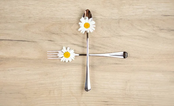 Sano concetto di alimentazione, vista dall'alto di cucchiaio e forchetta con fiori margherita al centro del tavolo in legno — Foto Stock