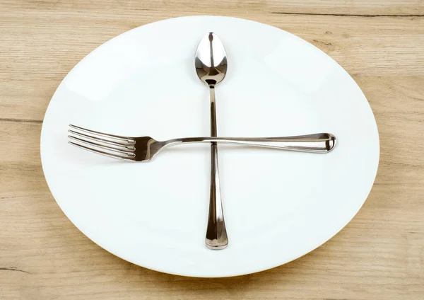 Κενό πιάτο με σταυρό πιρούνι και κουτάλι σε ξύλινο τραπέζι — Φωτογραφία Αρχείου