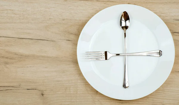 Placa vacía con tenedor de plata cruzado y cuchara sobre mesa de madera. Vista superior con espacio de copia . —  Fotos de Stock