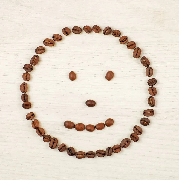 Smiley face made of coffee beans on wooden background. Square image