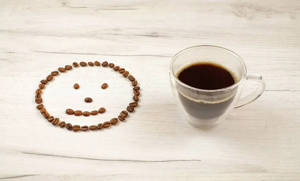 Cara sonriente hecha con granos de café y taza de café negro sobre fondo de madera — Foto de Stock