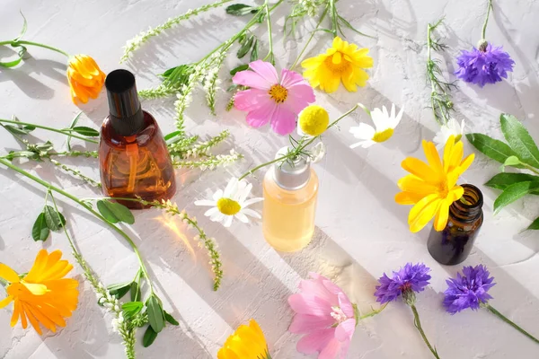 Botellas con ingredientes farmacéuticos naturales y flores coloridas con luz solar sobre fondo blanco —  Fotos de Stock