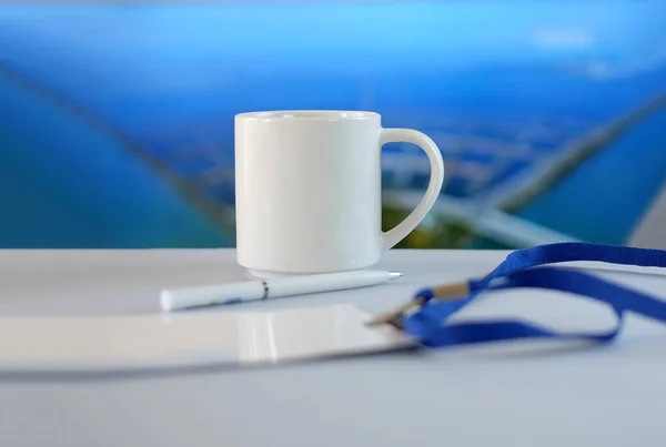 White cup, badge and pen on white table, soft blue background — Stock Photo, Image