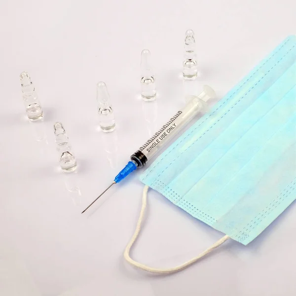 Seringue, masque bleu médical et ampoules sur fond blanc. Concept de vaccination — Photo