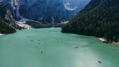 Tepe manzaralı dağ manzarası. Yüksek uçurum ağaçları, orman ve ortasında mavi bir göl olan kayıklı bir manzara..