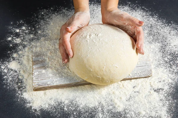 Pizza dough or baking on a dark black background of wood. Baking bread, pizza, pasta. Top view, horizontal photo