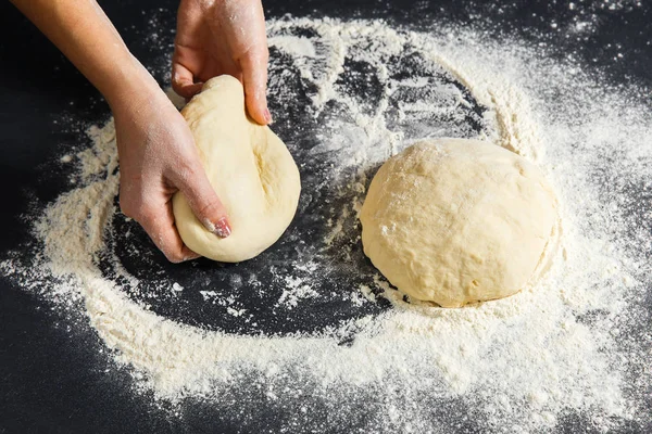 Pizza dough or baking on a dark black background of wood. Baking bread, pizza, pasta. Top view, horizontal photo