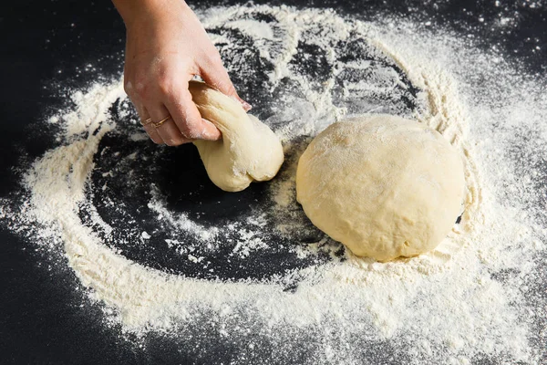 Pizza dough or baking on a dark black background of wood. Baking bread, pizza, pasta. Top view, horizontal photo