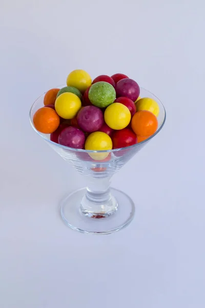 Gri arka planda şeffaf cam kasede renkli şekerler.