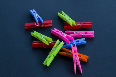 Siyah arkaplanda renkli plastik çamaşır mandalları var..