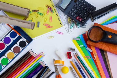 Beyaz yüzeyde renkli okul malzemeleri var..