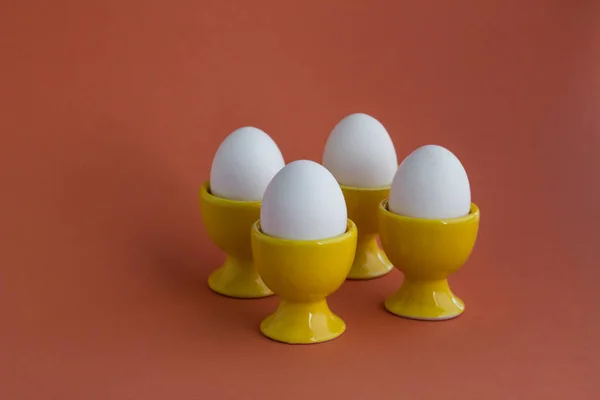 Sarı renkli yumurta tutacağında dört haşlanmış yumurta. Pembe arka planda fotokopi alanı var.
