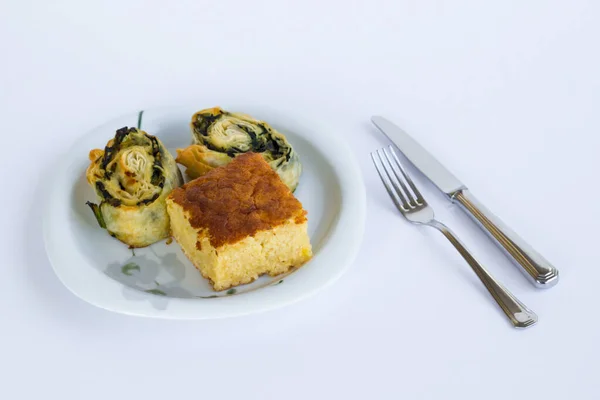 Bir dilim tatlı kek ve ıspanaklı turta siyah bir tabakta çatal bıçak setiyle..