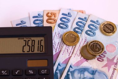 Beyaz yüzey üzerinde siyah renk hesap makinesi ve sikkelerle Türk banknotları. Yukarıdan çekilmiş.