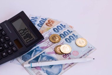 Beyaz yüzey üzerinde siyah renk hesap makinesi ve sikkelerle Türk banknotları. Yukarıdan çekilmiş.