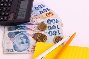 Beyaz yüzey üzerinde siyah renk hesap makinesi ve sikkelerle Türk banknotları. Yukarıdan çekilmiş.