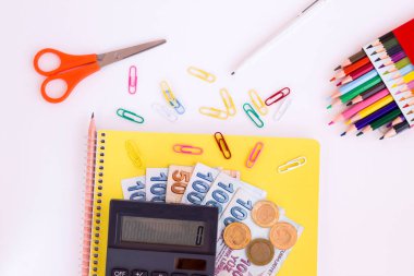 Hesap makinesi ve Türk parasıyla beyaz yüzey üzerinde renkli okul malzemeleri. Okul giderlerinin kavramsal görüntüsü.