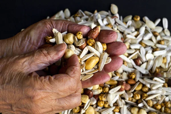 Fresh nuts in hand of unknown old person  on blurred nuts background,top view