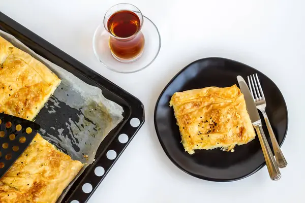 Geleneksel Türk ev yapımı hamur işi, metal tepsi içinde, tabak, çatal bıçak seti ve çay ile beyaz tepside dilimlenmiş.