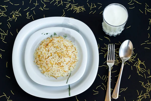 Geleneksel Türk pirinci, tereyağlı içecek ve çatal bıçak setiyle siyah yüzeye dizilmiş vermicelli ile pişiriliyor.