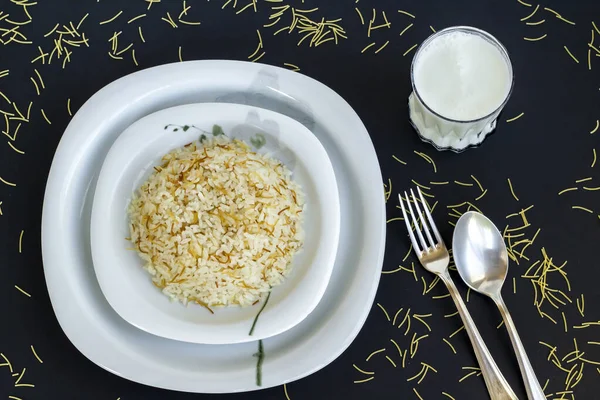 Traditional Turkish rice cooked with vermicelli,designed on black surface with buttermilk drink and cutlery set