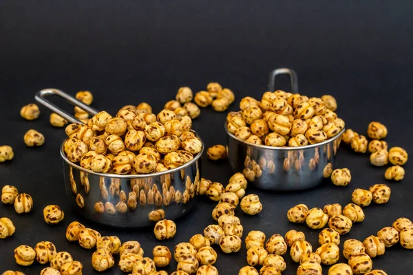 Siyah zemin üzerinde küçük paslanmaz çelik kaplar olan sarı nohutlar.. 