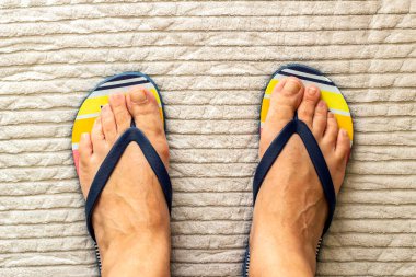 El dokuması halıda parmak arası terlik giyen bir çift ayak.