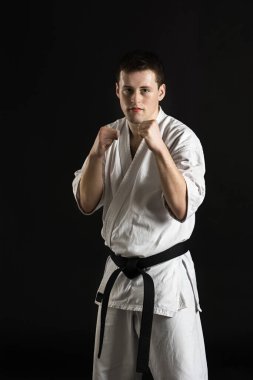 Bir karateka vurur ya da bir duruşta durur. Dövüş sanatları. Shidokan karatesi. Stüdyoda dövüşçü var. Siyah arka planda kimonolu adam. Yumruk at. Tekmele. Dünya Karate Birliği, Shidokan. Kara kuşak karate.