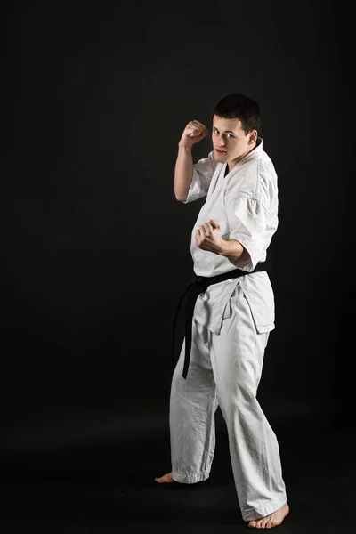 Bir karateka vurur ya da bir duruşta durur. Dövüş sanatları. Shidokan karatesi. Stüdyoda dövüşçü var. Siyah arka planda kimonolu adam. Yumruk at. Tekmele. Dünya Karate Birliği, Shidokan. Kara kuşak karate.
