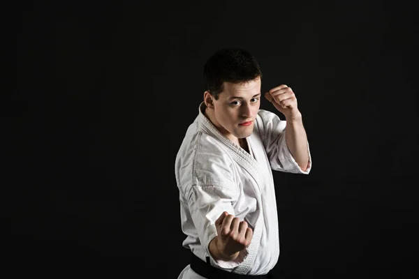 Bir karateka vurur ya da bir duruşta durur. Dövüş sanatları. Shidokan karatesi. Stüdyoda dövüşçü var. Siyah arka planda kimonolu adam. Yumruk at. Tekmele. Dünya Karate Birliği, Shidokan. Kara kuşak karate.