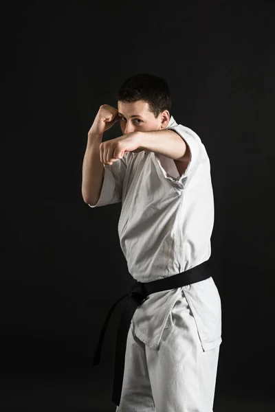 Bir karateka vurur ya da bir duruşta durur. Dövüş sanatları. Shidokan karatesi. Stüdyoda dövüşçü var. Siyah arka planda kimonolu adam. Yumruk at. Tekmele. Dünya Karate Birliği, Shidokan. Kara kuşak karate.