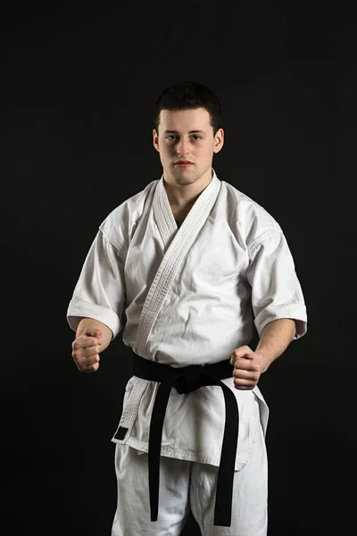 Bir karateka vurur ya da bir duruşta durur. Dövüş sanatları. Shidokan karatesi. Stüdyoda dövüşçü var. Siyah arka planda kimonolu adam. Yumruk at. Tekmele. Dünya Karate Birliği, Shidokan. Kara kuşak karate.