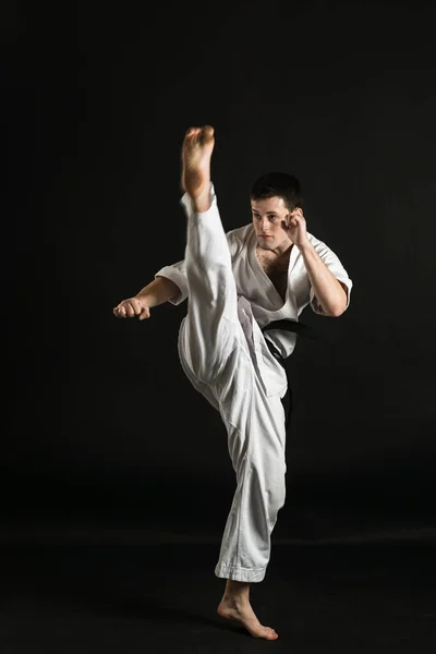 A karateka strikes or stands in a stance. Martial arts. Shidokan karate. Fighter in the studio. Kimono guy on a black background. Punch. Kick. World Karate Association the Shidokan. Black belt karate.